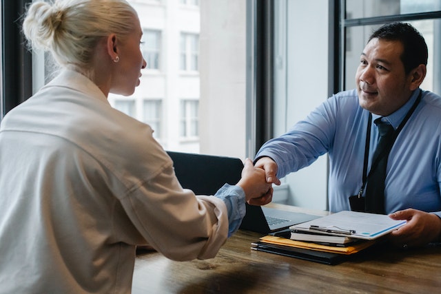 Two people in business dress shaking hands over a desk.